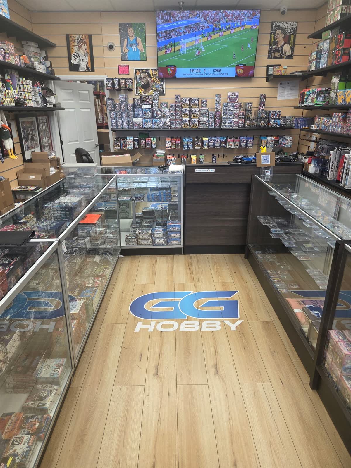 Inside GG Hobby in Aventura — the GG logo on the floor between glass display cases of slabs and a wall of hobby boxes